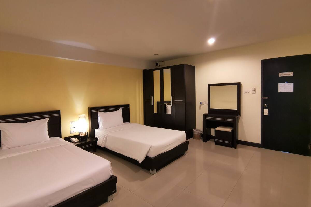 A hotel room with two beds, a wardrobe, a vanity with a mirror, and a door with a sign.