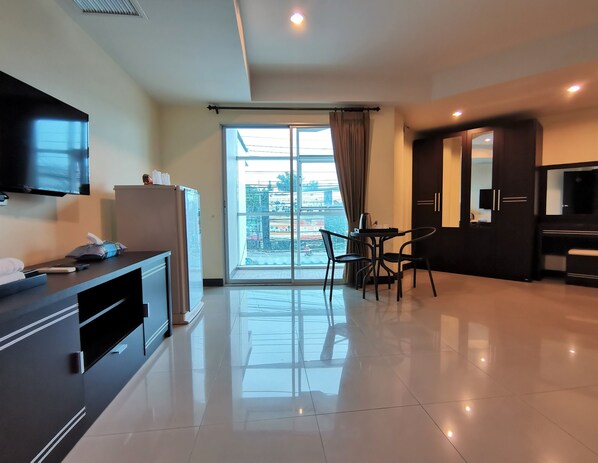 Una habitación de hotel moderna con televisión de pantalla plana, refrigerador, zona de comedor con mesa y sillas, y un ventanal con cortinas.