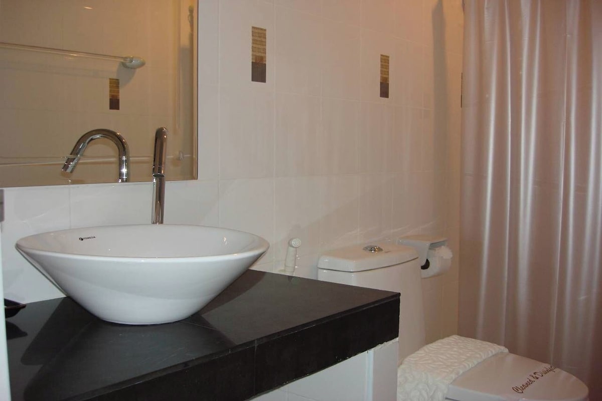 Une salle de bain avec un lavabo blanc, un miroir, des toilettes et un rideau de douche.