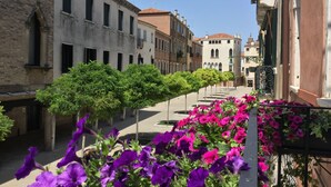 Una stretta via fiancheggiata da edifici storici, alberi e fiori colorati.