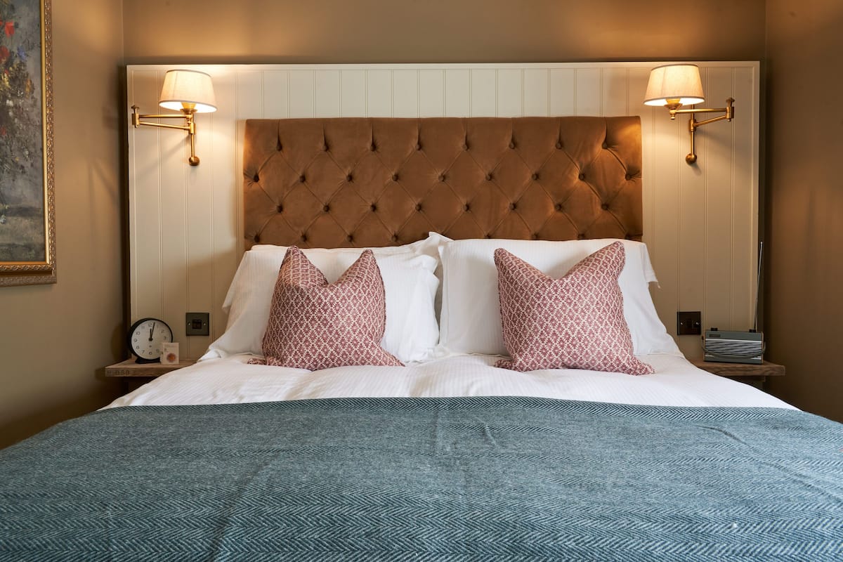 A neatly made bed with a tufted headboard, two bedside lamps, and a clock on a nightstand.