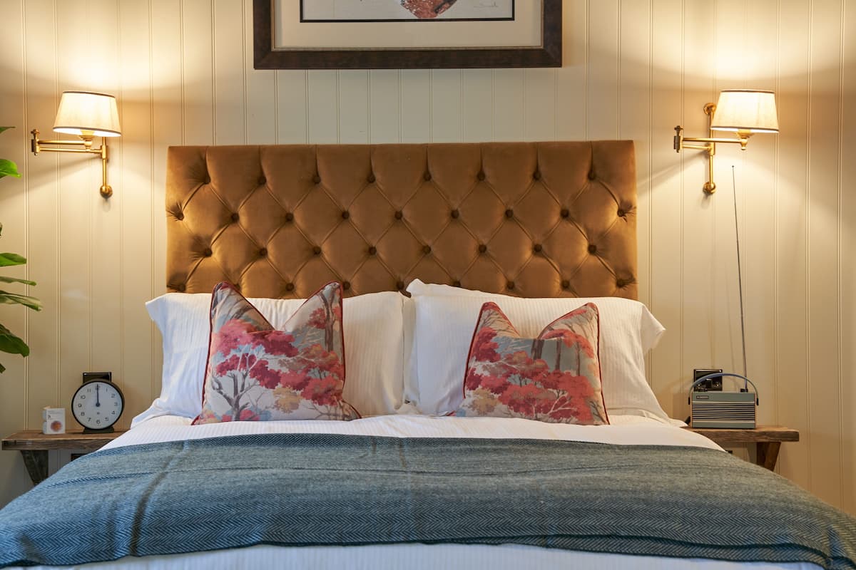 A bedroom with a tufted headboard, floral pillows, a clock, and bedside lamps.