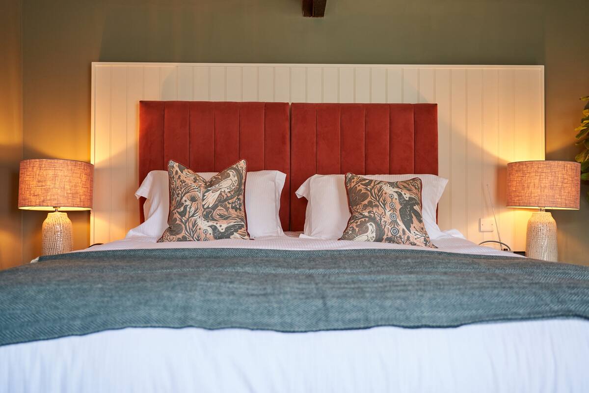 A neatly made bed with a red headboard, white bedding, and patterned pillows. There are two bedside lamps with lampshades.