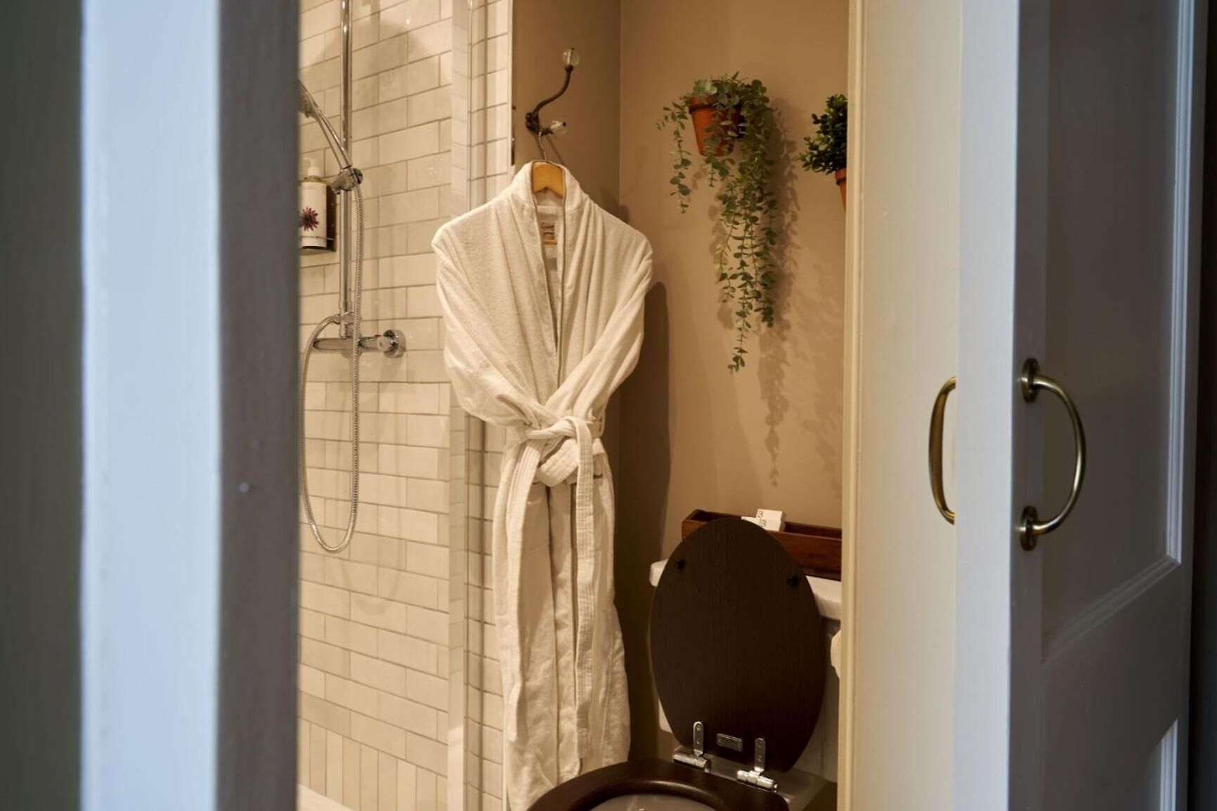 Un baño con ducha, inodoro y una bata colgada en la pared.