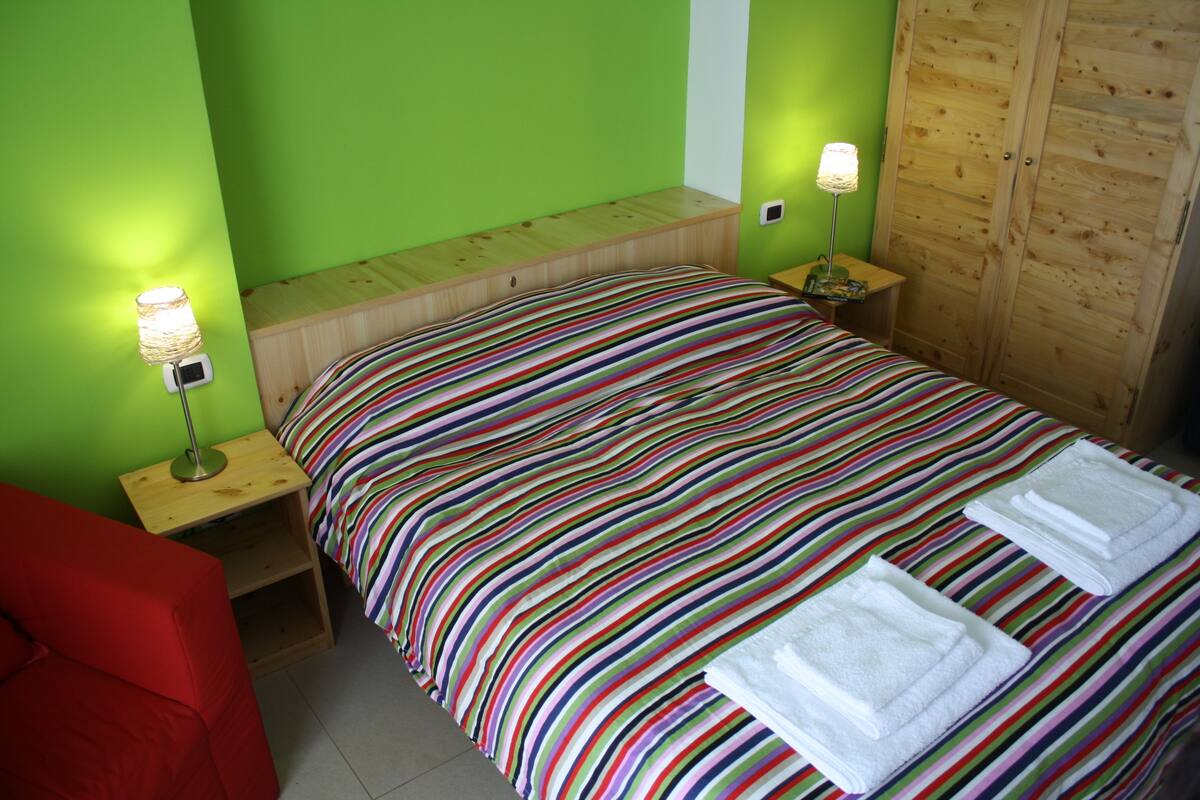 A room with a bed, two bedside tables, a red chair, and a wooden wardrobe.