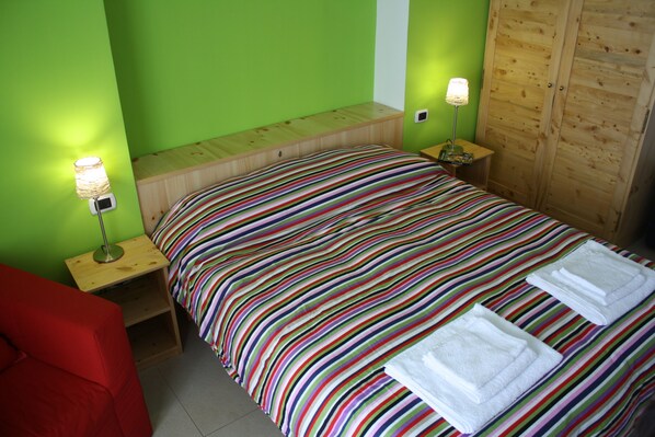 A room with a bed, two bedside tables, a red chair, and a wooden wardrobe.
