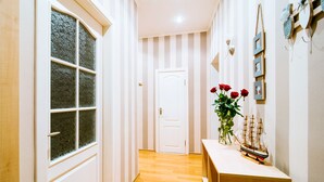 Ein Korridor mit Holzboden, einer weißen Tür am Ende und einem Holztisch mit einem Schiffmodell und roten Rosen.
