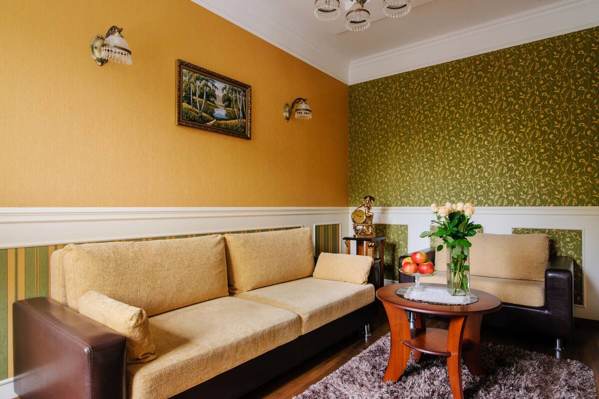 Una sala de estar con un sofá, una mesita redonda con un florero y fruta, y un cuadro en la pared.