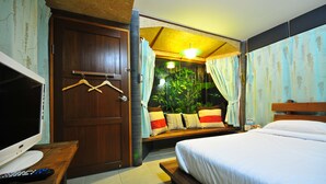 A hotel room with a bed, a TV, a desk with a remote control, a wooden bench, and a window with curtains. - Cafe'@luv22 (Wichit)