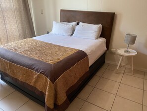Una cama bien hecha con una colcha estampada, un cabecero de madera y almohadas blancas.