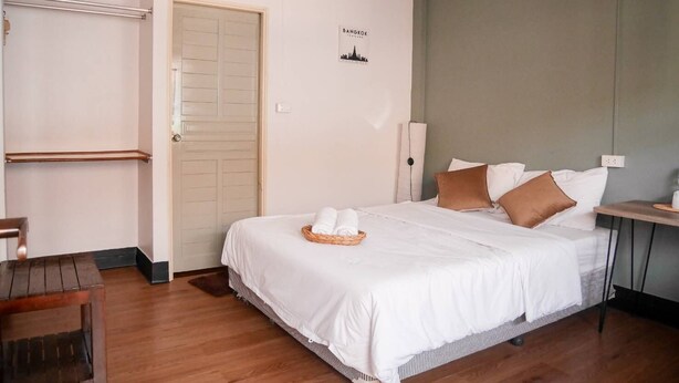 A neatly arranged bedroom with a bed, a bedside table, a chair, and a door. - Orchid House (Chiang Rai)