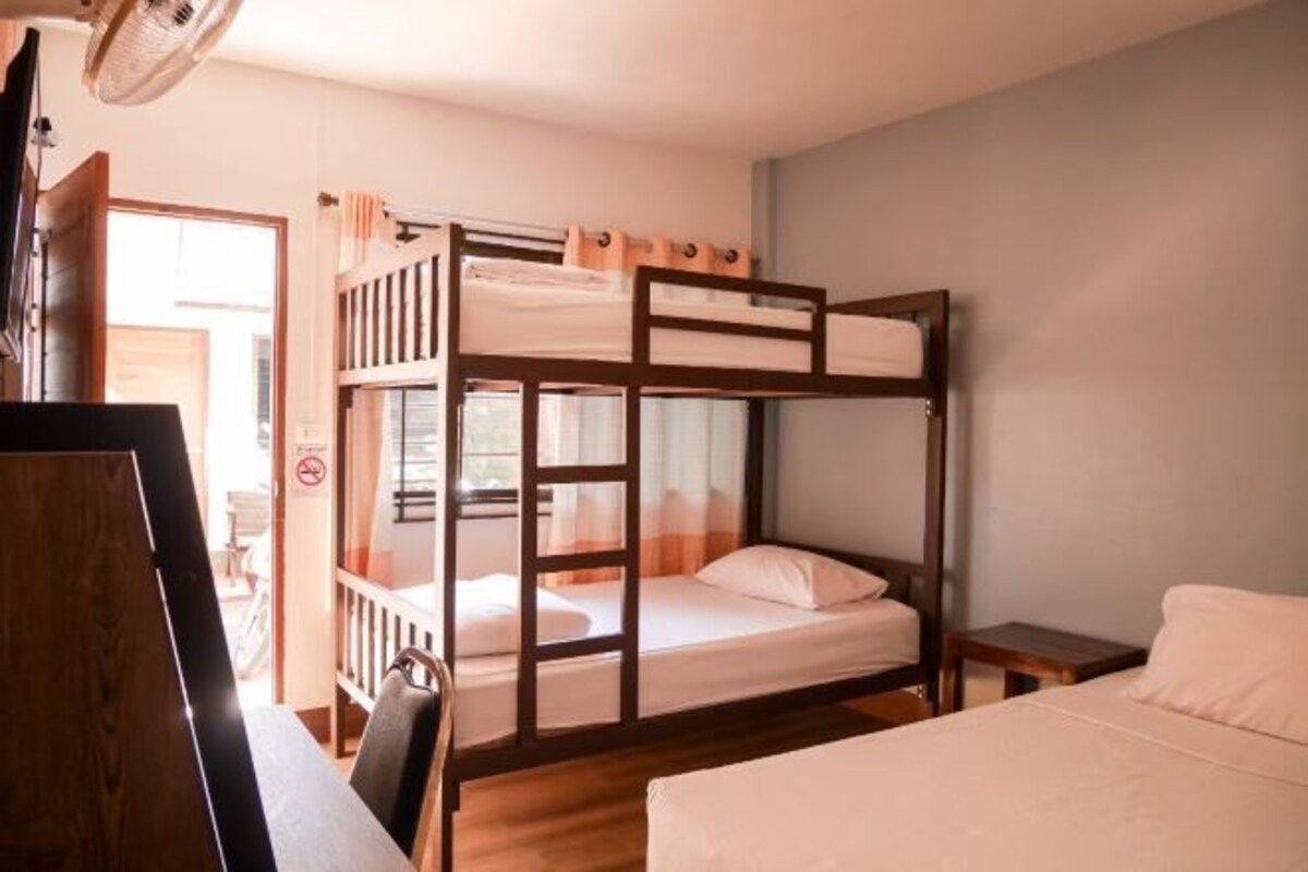 A bunk bed room with a desk and chair, a small table, and a window with curtains.