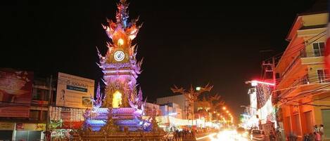 A night scene with a brightly lit pagoda-like structure with a clock, surrounded by a decorative moat and palm trees.