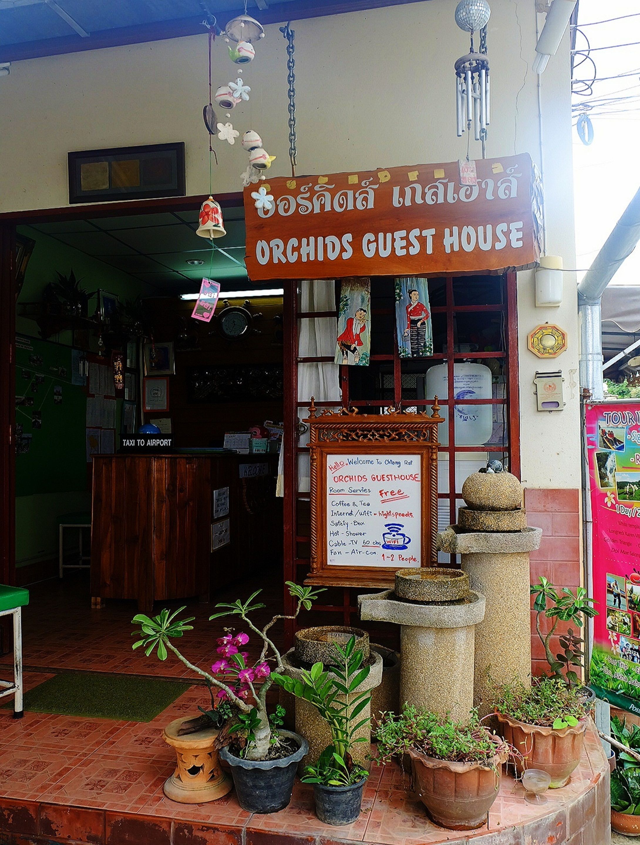 Fachada de Orchids Guest House con un cartel, un mensaje de bienvenida y una lista de servicios.
