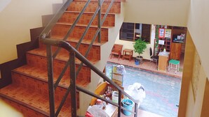 A staircase leading to a ground floor with a small seating area, a plant, and a sign indicating a rental service. - Orchid House (Chiang Rai)