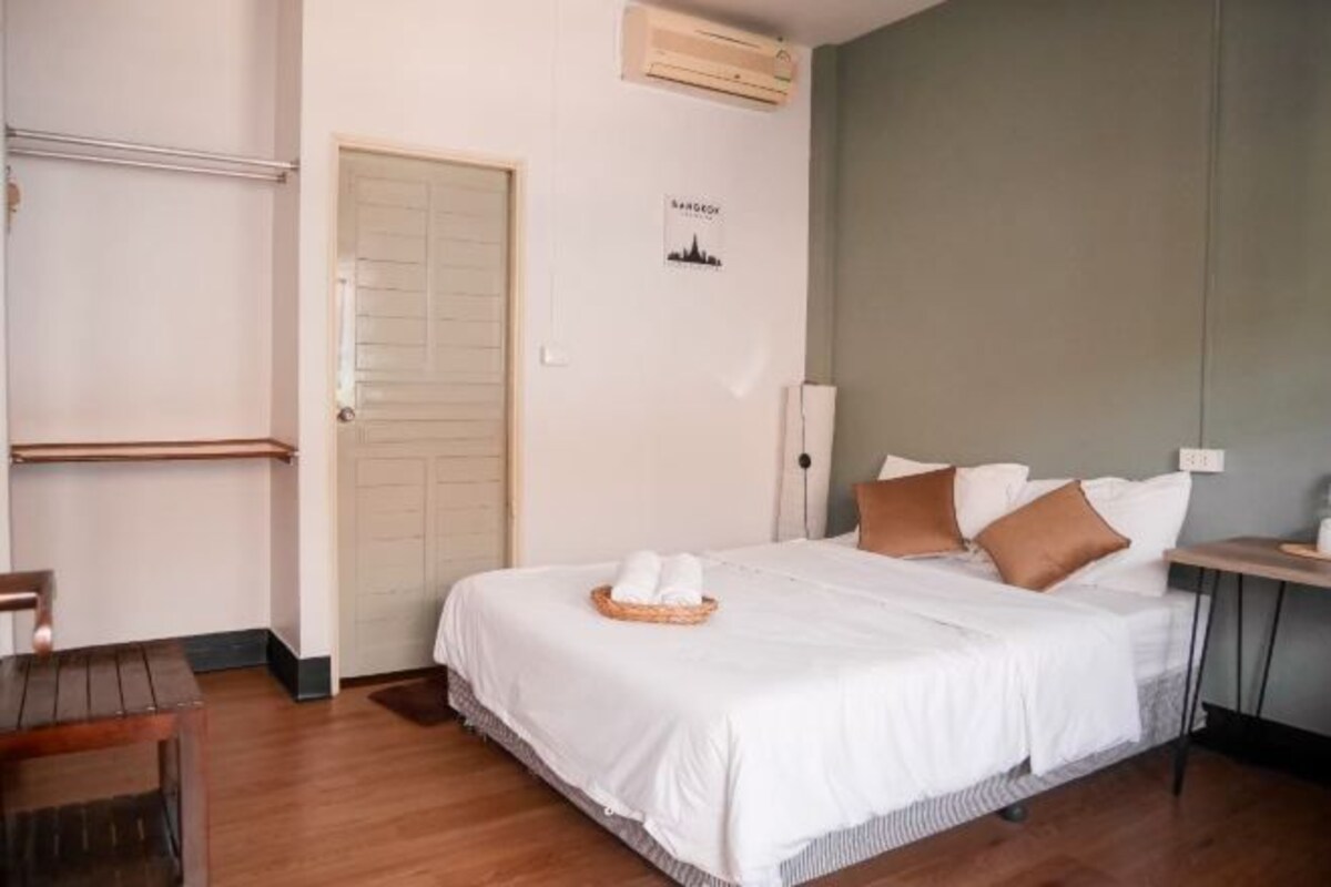 A neatly arranged bedroom with a bed, a bedside table, a chair, and a wall-mounted shelf.