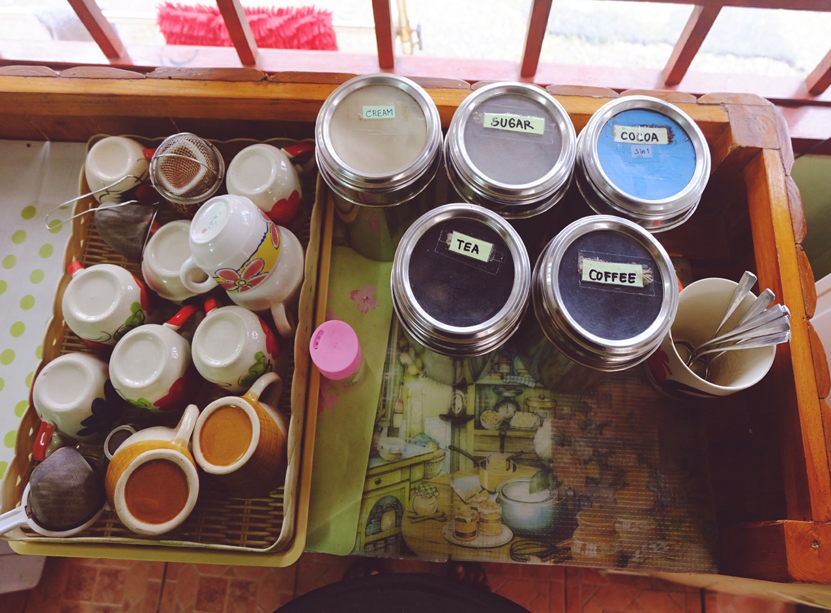 A tray with various containers labeled with different types of beverages and a collection of colorful cups and saucers.