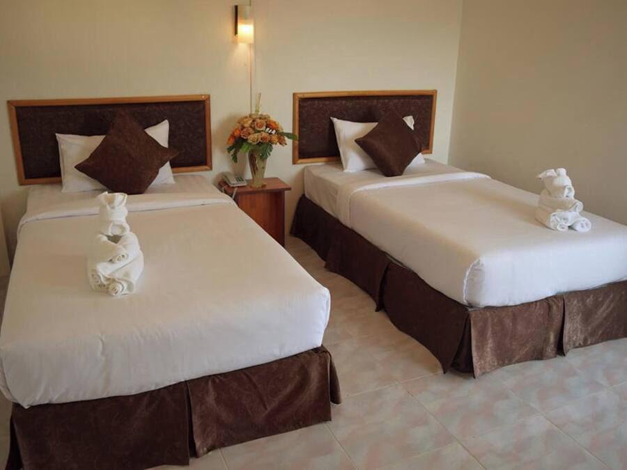 Habitación de hotel con dos camas, cada una con cabecero marrón, ropa de cama blanca y una toalla sobre la cama.