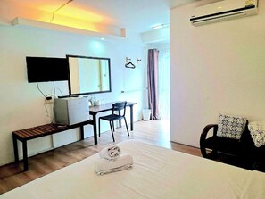 A hotel room with a bed, a desk, a chair, a television, and an air conditioning unit. - Hotel De Ratt (Ratsada)