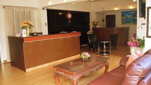 A hotel lobby with a reception desk, a wooden coffee table, a leather sofa, and a dining area with chairs. - Hotel De Ratt (Ratsada)