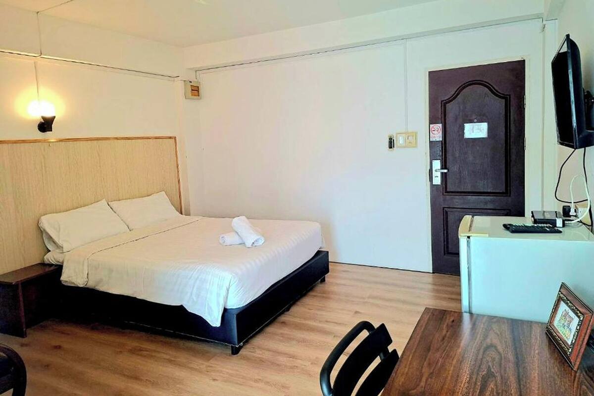 A hotel room with a bed, bedside table, desk, chair, and a television.
