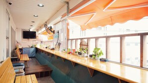 Un restaurante con bancos y mesas de madera, una barra con plantas y un televisor montado en la pared.