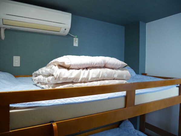 A bunk bed with a mattress and pillows, a power outlet, and an air conditioning unit on the wall.