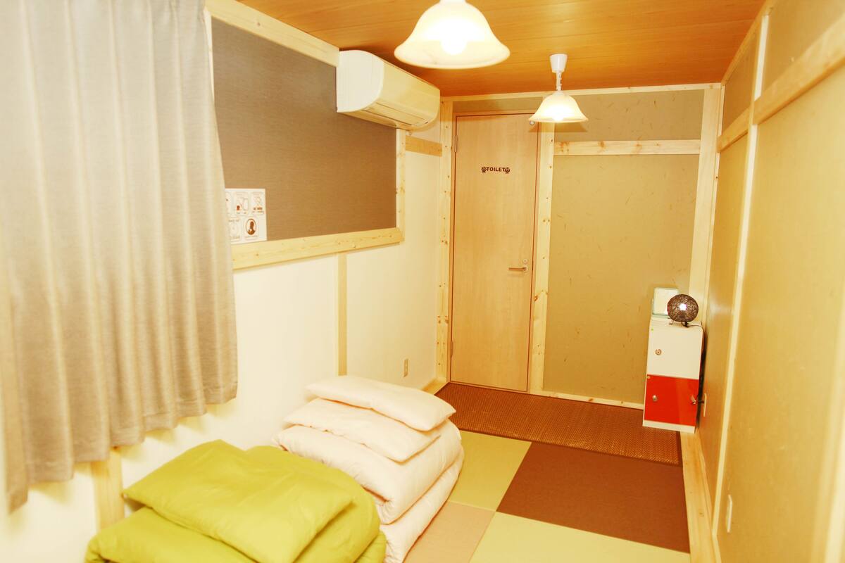 A small, cozy room with a bed, pillows, a wooden door, and a small heater.