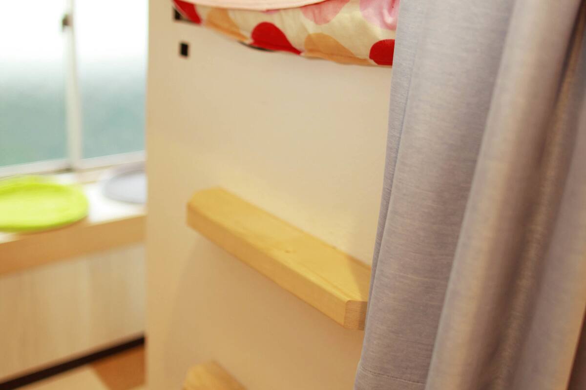 A bunk bed with a window, a wooden shelf, and a grey curtain.