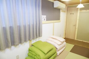 Ein Zimmer mit einem Bett, einem Vorhangfenster, einer Tür mit der Aufschrift „TOILET“ und einer Wand-Klimaanlage.