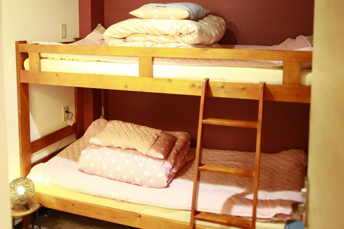 A bunk bed room with a ladder, a small table, and a trash bin.