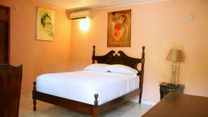 Quarto com cama de madeira, mesa de cabeceira, luminária e duas pinturas na parede.
