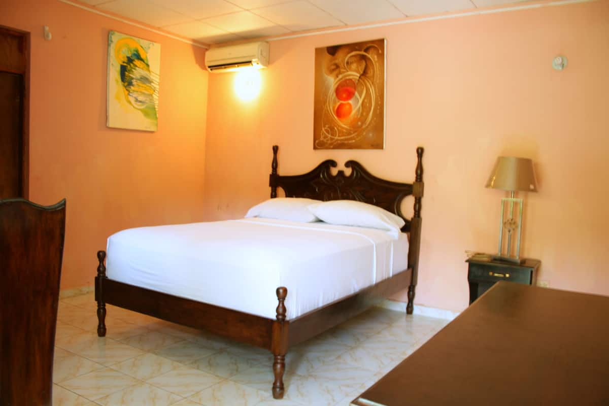 Une chambre à coucher avec un lit en bois, une table de chevet, une lampe et deux tableaux accrochés au mur.
