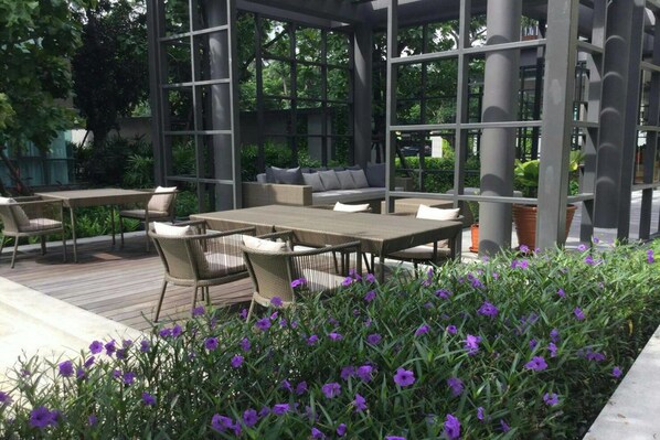 An outdoor patio with a wooden deck, wicker furniture, and a garden with purple flowers.