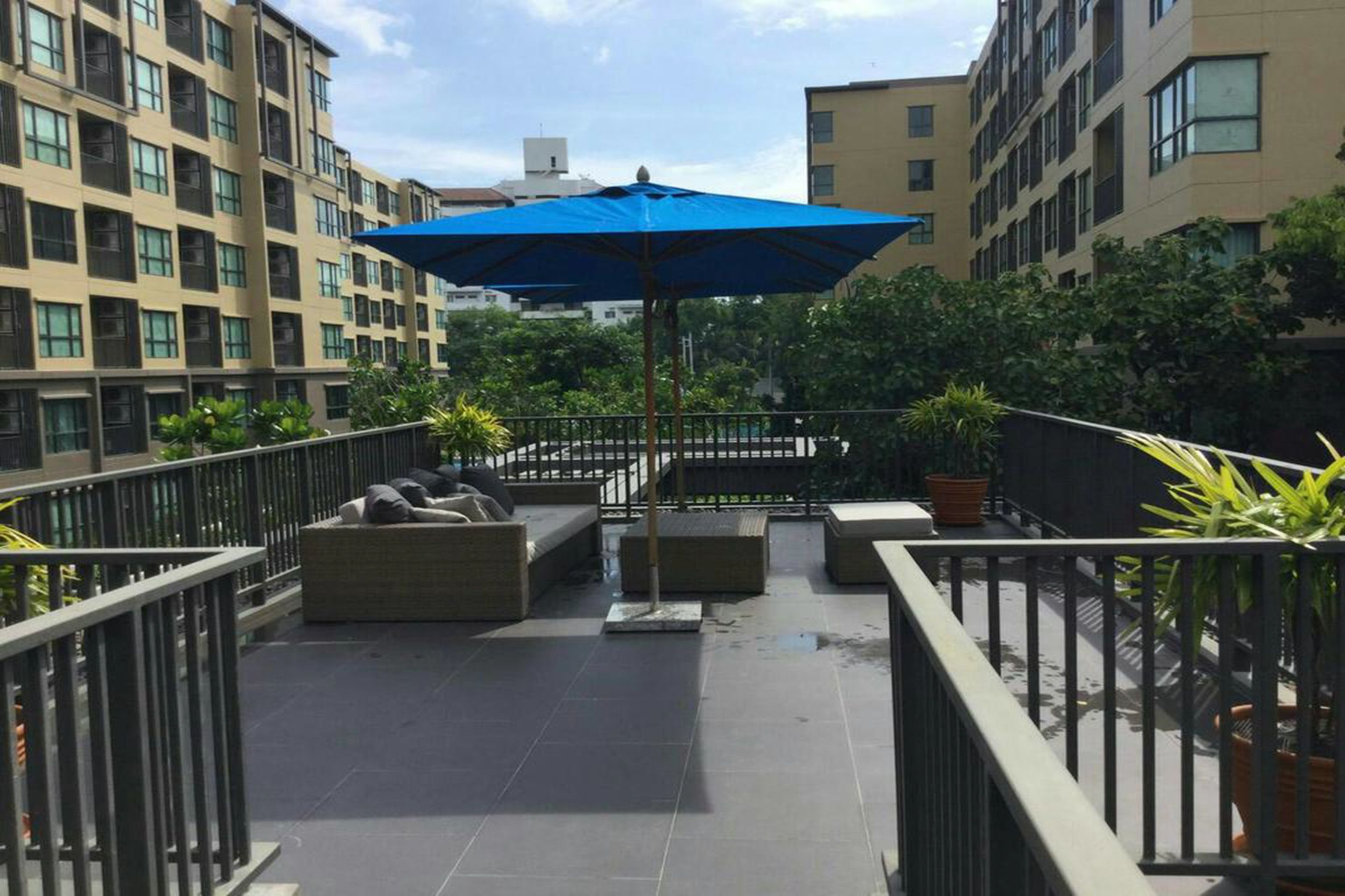 A rooftop terrace with outdoor seating, a blue umbrella, and potted plants.