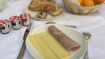 A table set with a plate of sliced cheese, a wrapped ham, and condiments.