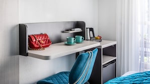 A hotel room with a bed, a desk with a chair, a TV, a window with curtains, and a red handbag on the desk. - Hotel Jardin Croisette (Cannes)