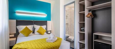 A modern hotel room with a bed, a walk-in closet, and a bathroom.