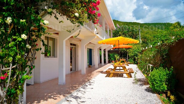 Un bâtiment blanc doté d’un patio couvert, d’un parasol jaune et d’un chemin de gravier.