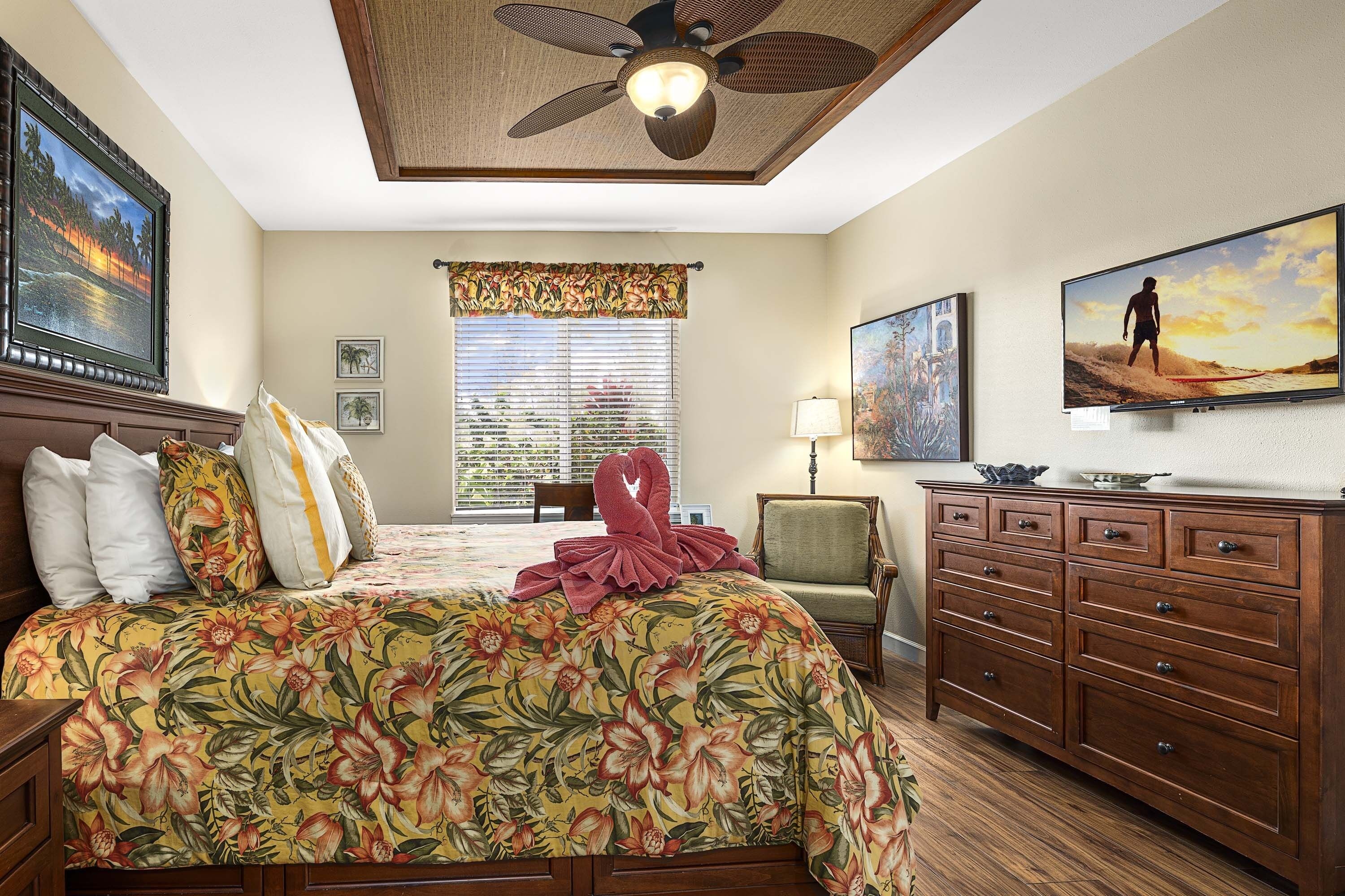 A hotel room with a bed, a wooden dresser, a ceiling fan, and artwork on the walls.