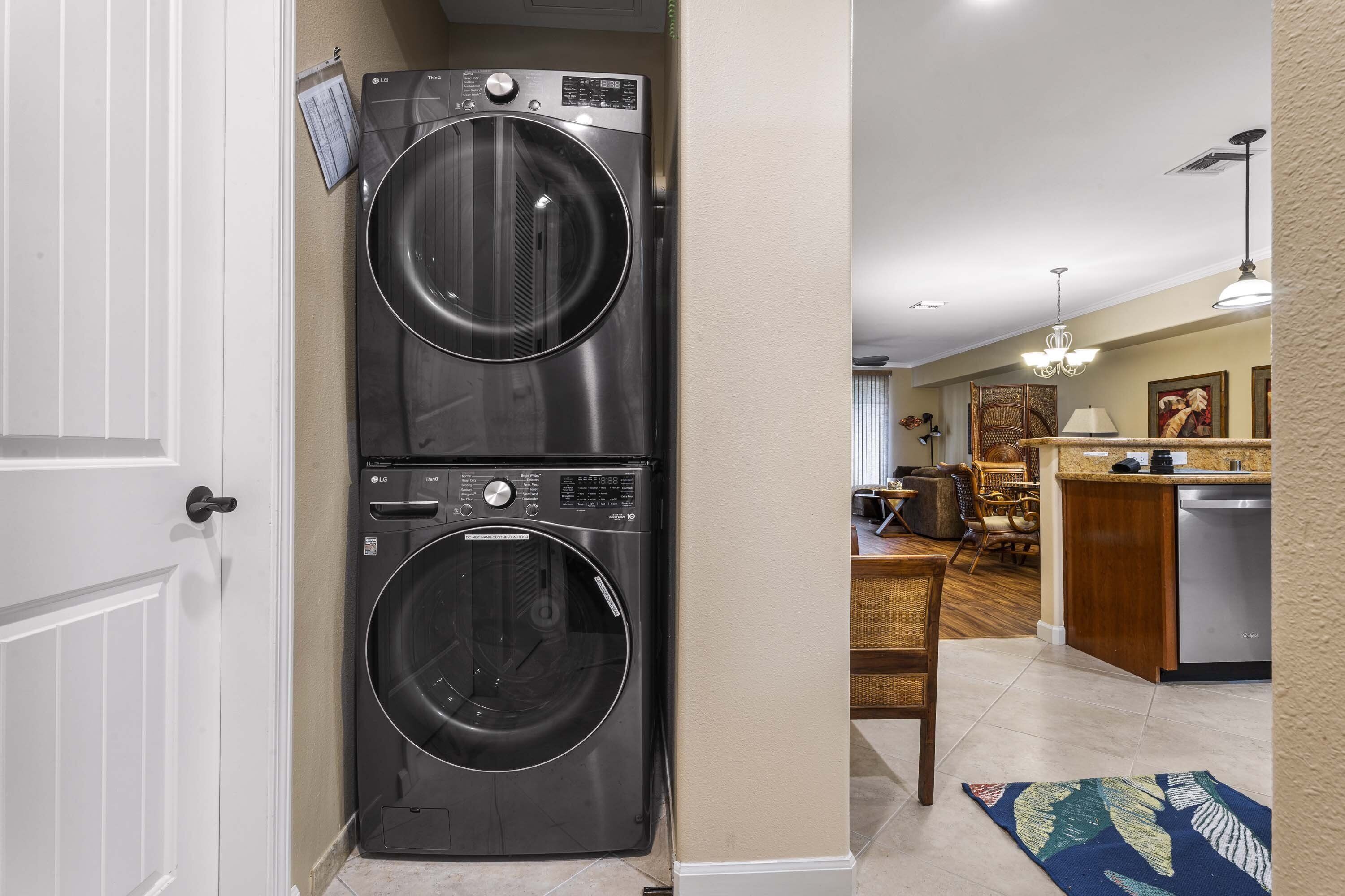 A laundry room with two stacked front-loading washers and dryers, a kitchen area with a dishwasher, and a dining area with a table and chairs.