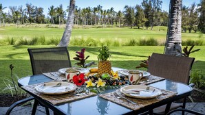 Ein Tisch im Freien mit Blick auf eine tropische Landschaft, dekoriert mit einer Ananas, Früchten und einem Blumenarrangement.