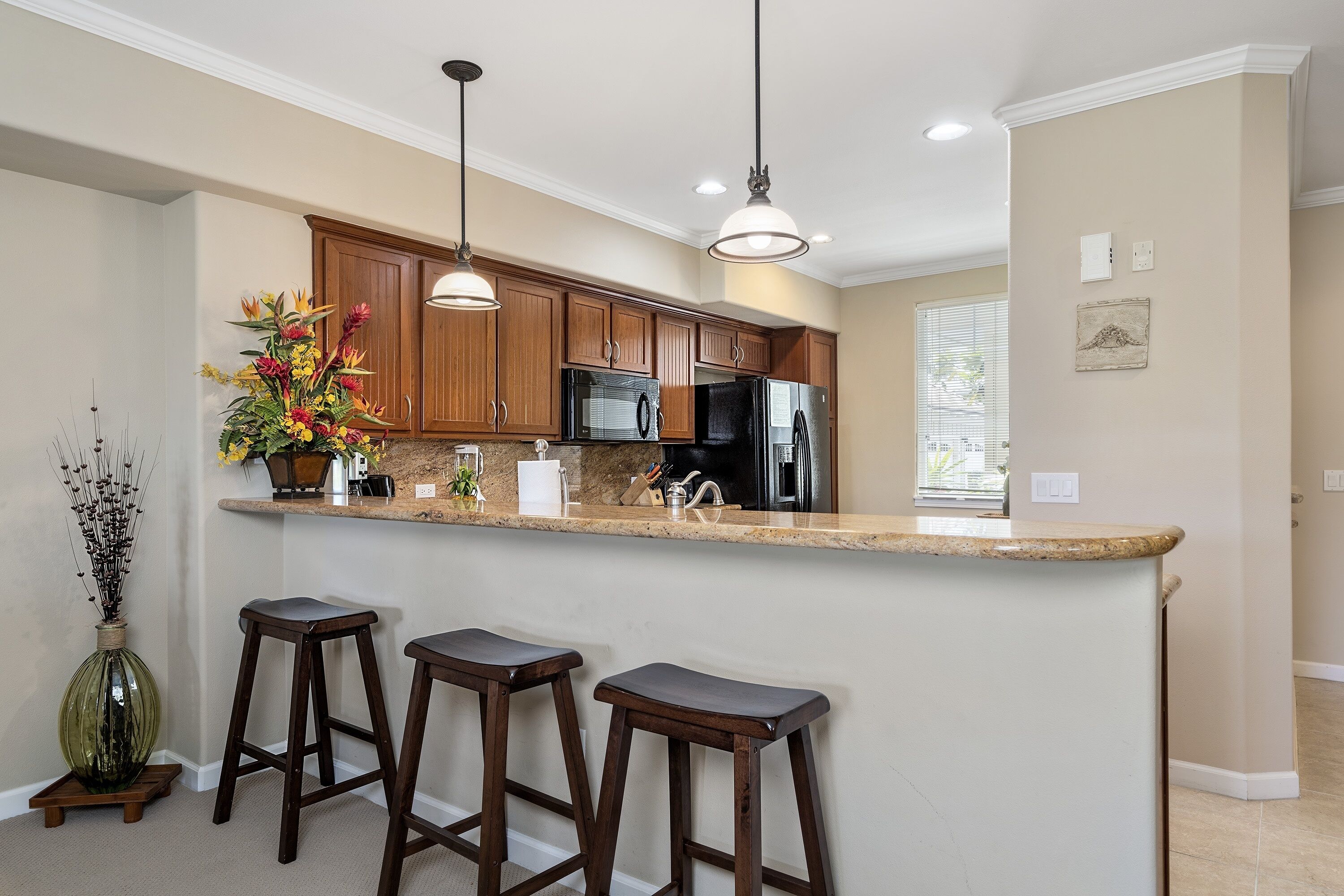 A kitchen with wooden cabinets, a granite countertop, and three bar stools.
