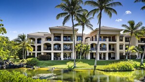 A multi-story hotel with a pool, palm trees, and a well-maintained lawn.