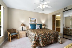 A bedroom with a bed, a chair, a nightstand, a ceiling fan, and a large mirror. - Shores At Waikoloa #234 At Bo Tree Tower 2 Bedroom Condo by RedAwning (Waikoloa)