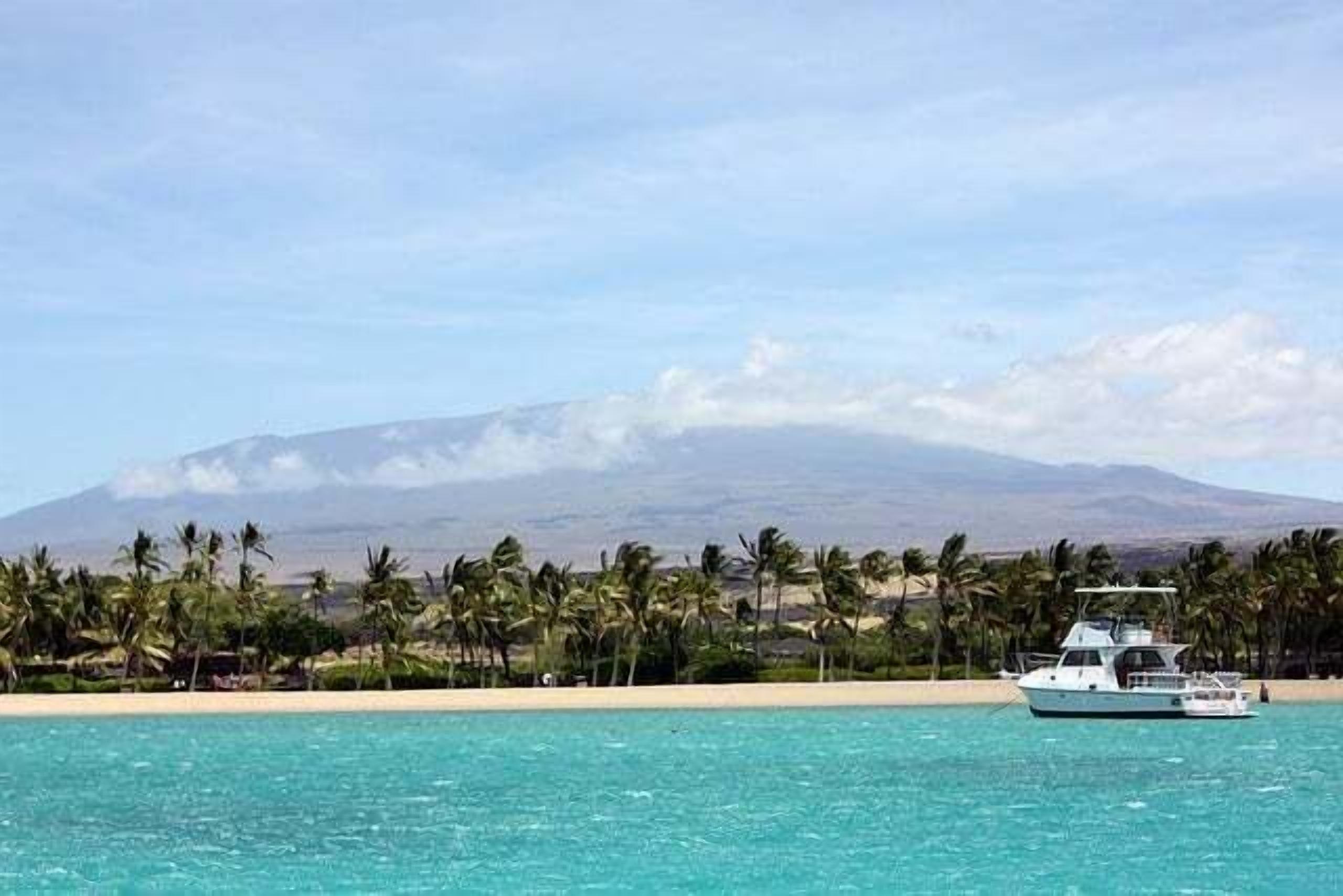 A boat on turquoise water with a mountain and palm trees in the background.