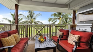 A covered outdoor seating area with red sofas and a table with fruit. - Waikoloa Beach S H32 2 Bedroom Condo by RedAwning (Waikoloa)