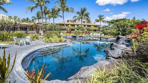 Ein Resort-Pool mit tropischer Bepflanzung, einem überdachten Sitzbereich und einem Gebäude mit Balkonen.