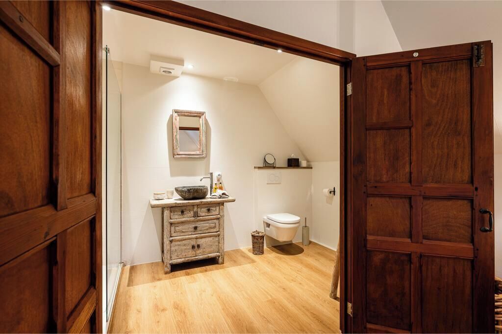 A bathroom with a wooden vanity, a sink, a mirror, a toilet, and a wooden door.