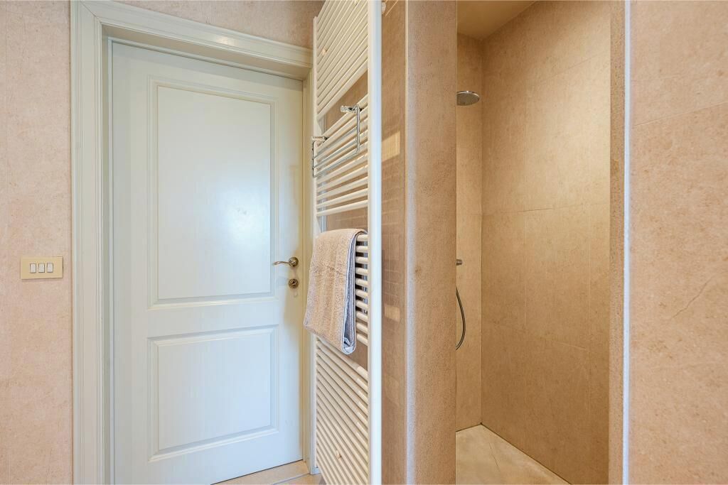 A bathroom with a white door, a towel rack with a towel, and a shower area with beige tiles.